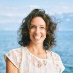 Outdoor close up portrait of happy candid woman, brown curly hair, big smile, posing with lakeside nature background