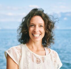 Outdoor close up portrait of happy candid woman, brown curly hair, big smile, posing with lakeside nature background