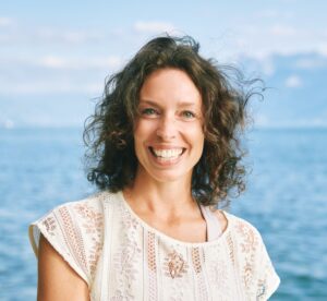 Outdoor close up portrait of happy candid woman, brown curly hair, big smile, posing with lakeside nature background