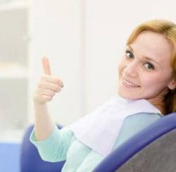 A woman in a dental chair giving a thumbs up.