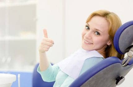 A woman in a dental chair giving a thumbs up.
