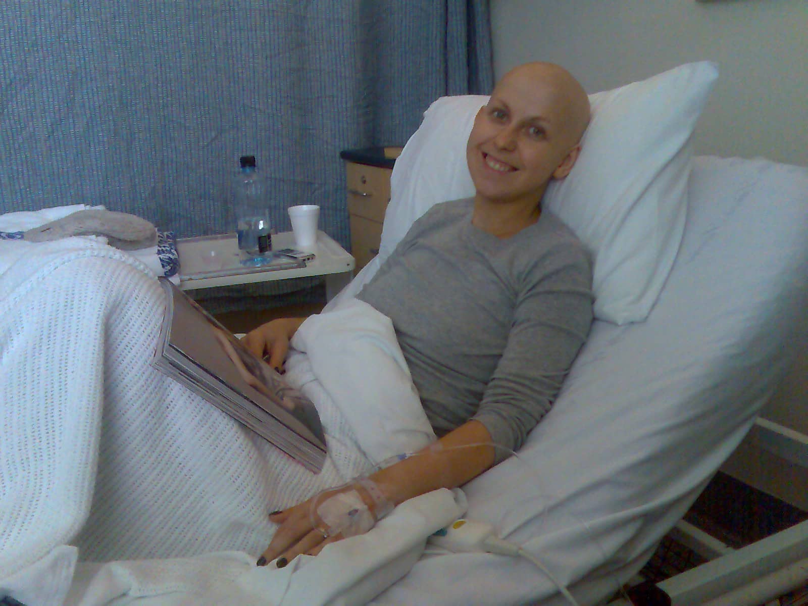 a cancer patient in a hospital bed smiling with a magazine on her lap